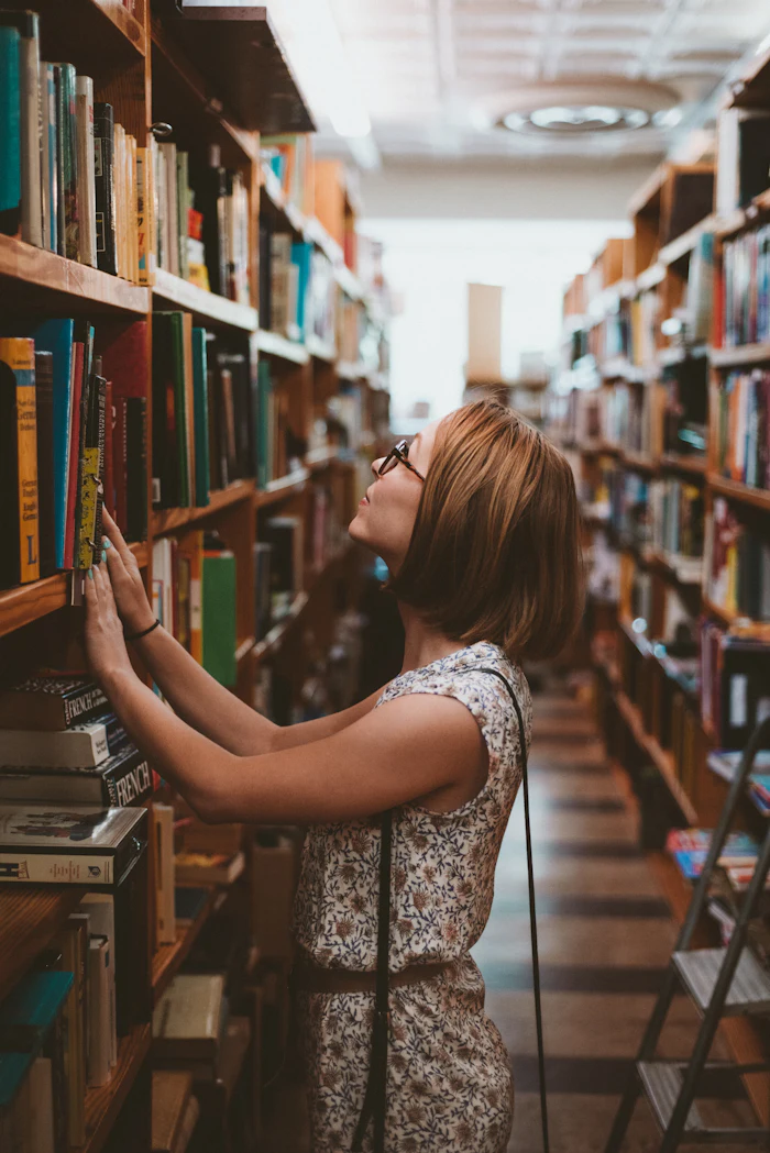 Mujer consultando un libro en los estantes de una biblioteca